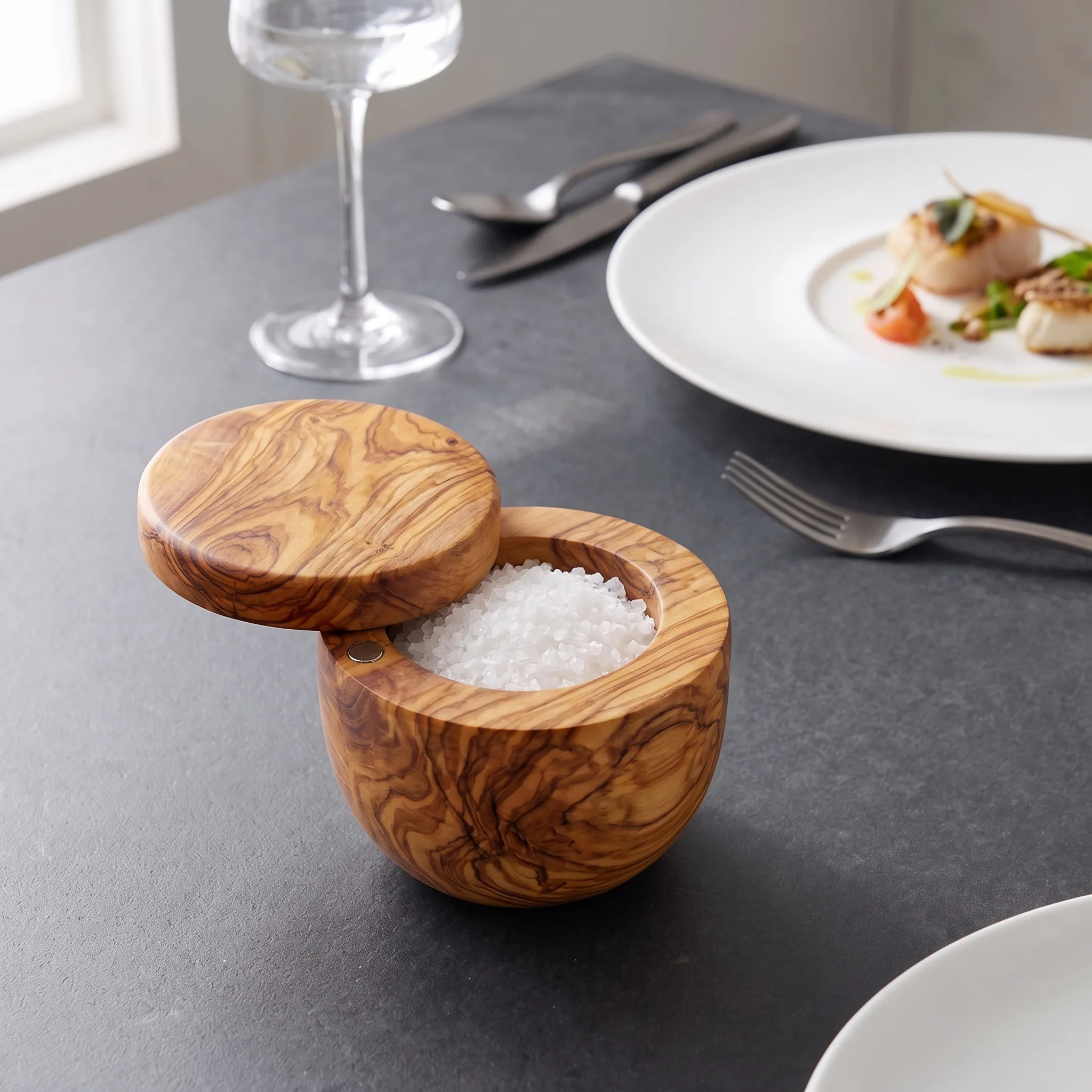 Open olive wood swivel-lid salt cellar on a dining table