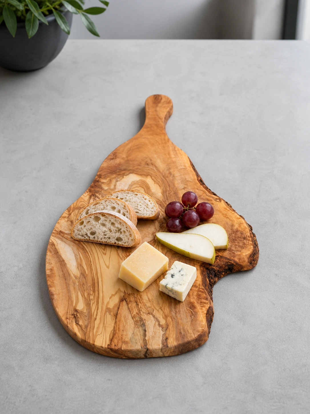 Planche palette en bois d’olivier présentant du pain, deux fromages, du raisin et des tranches de poire