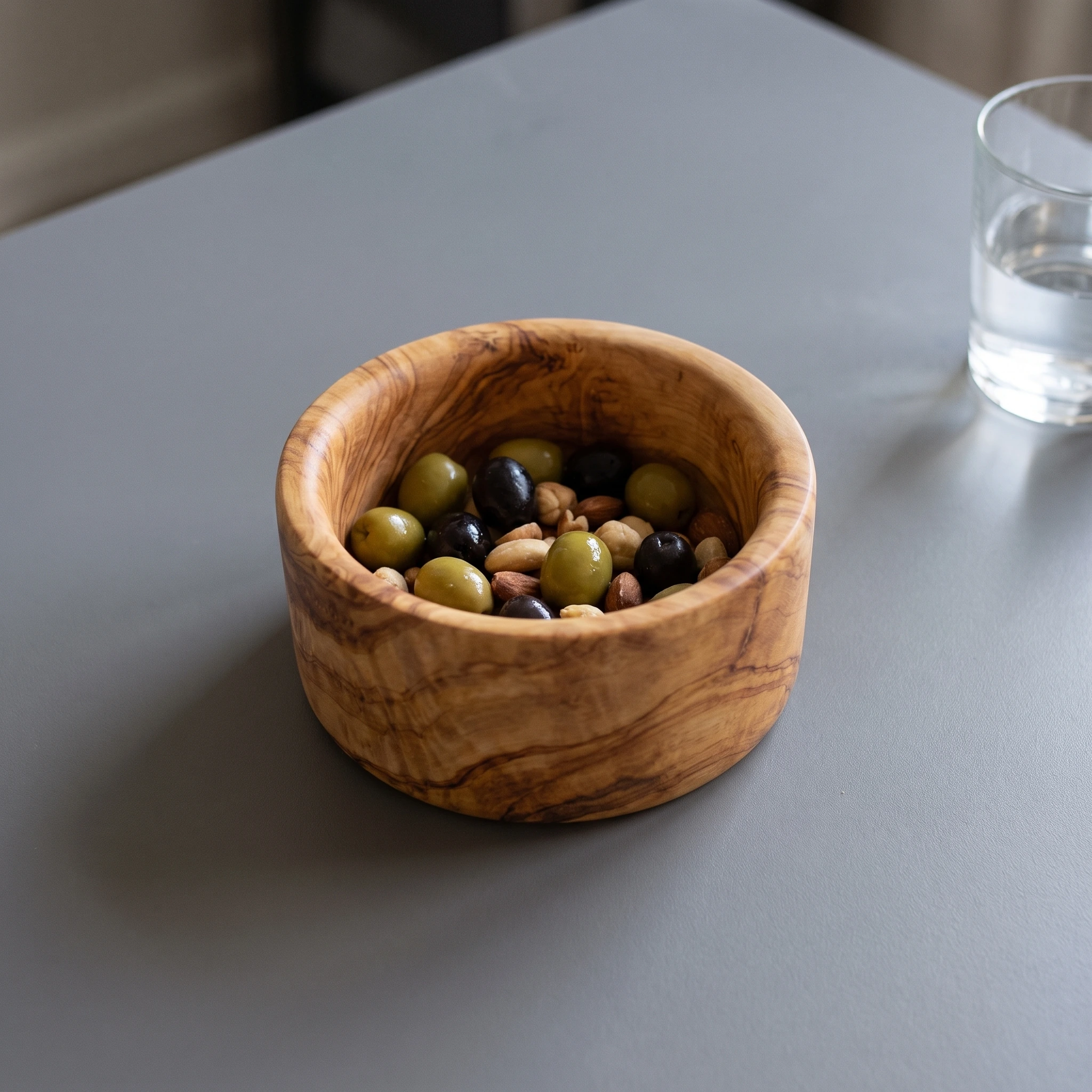 Petit bol apéritif en bois d’olivier avec olives et noix sur une table grise