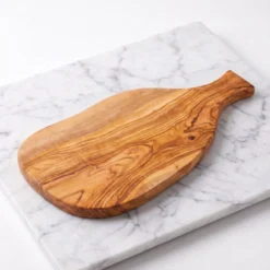 Planche à charcuterie en bois d'olivier CB-02 avec manche plein vue 3/4 studio au repos sur marbre blanc
