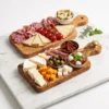 Deux planches en bois d’olivier garnies de fromage et charcuterie sur marbre blanc