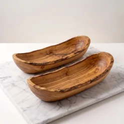 Two empty elongated olive wood bowls on light marble