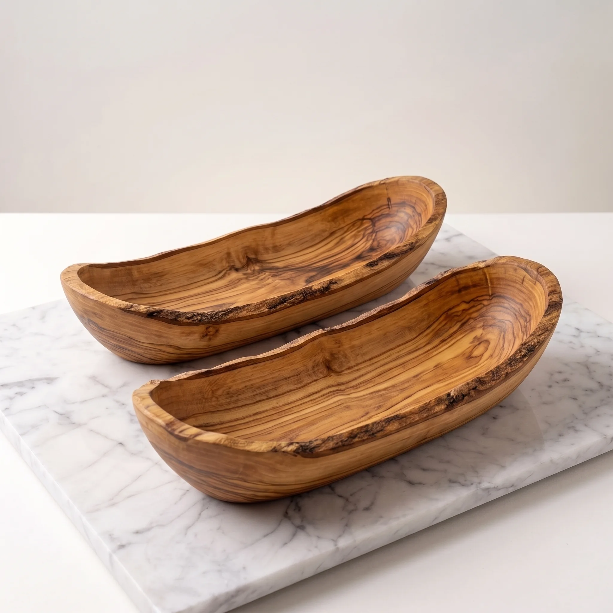 Two empty elongated olive wood bowls on light marble