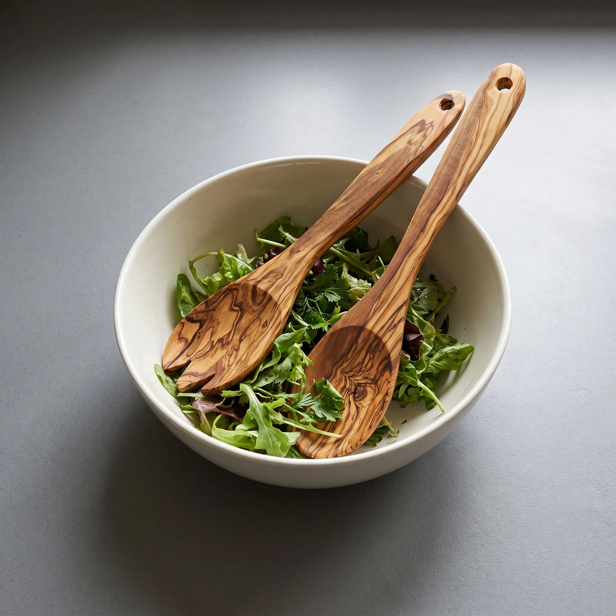 Olive wood salad servers in a bowl of green salad