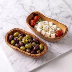 Deux raviers à tapas en bois d’olivier garnis d’olives et de feta sur marbre clair