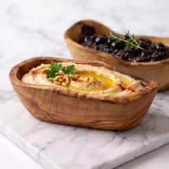 Two olive wood tapas bowls serving hummus and black olives