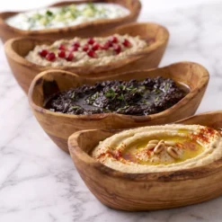 Four olive wood tapas bowls serving hummus, tapenade and other preparations