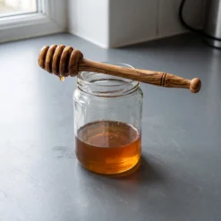 Olive wood honey dipper resting on a jar of honey