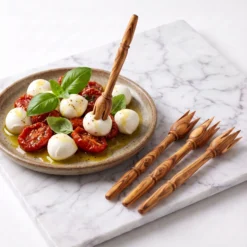 Un pic en bois d’olivier saisit une bouchée de mozzarella avec trois autres pics posés sur la table