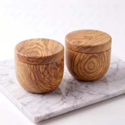 Two closed olive wood cellars on a light marble surface