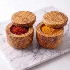 Deux boîtes en bois d’olivier ouvertes contenant du safran et du curcuma sur marbre clair