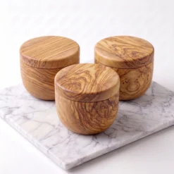 Three closed olive wood spice cellars on a light marble surface