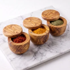 Trois boîtes en bois d’olivier ouvertes avec curcuma, safran et herbes séchées, vues sous un autre angle