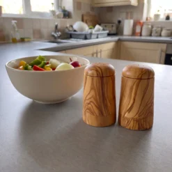 Olive wood salt and pepper shaker pair beside a bowl in the kitchen